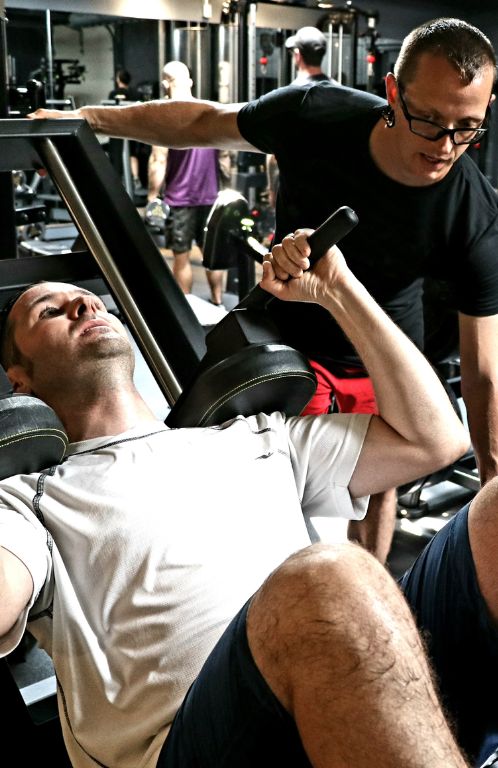 Coach Donovan spotting a male beginner client on the hack squat machine during strength training session.