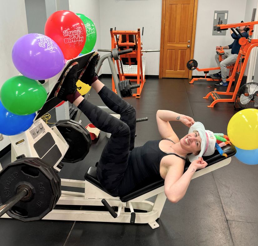 Female client in her 30s celebrating a personal record on the leg press during her birthday workout — showing strength, weight loss, and renewed energy from training with Coach Donovan.