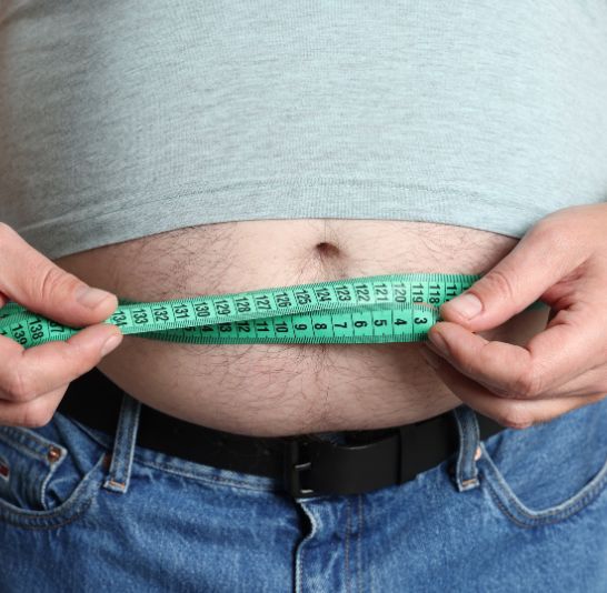 Close-up of a man wrapping a measuring tape around his belly to check his waist size for Coach Donovan’s body fat calculator.
