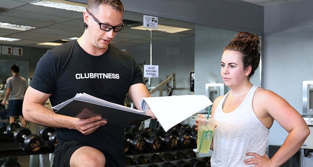 Coach Donovan reviewing a client’s workout plan and progress while explaining her training session — a personal, hands-on approach to fitness coaching.